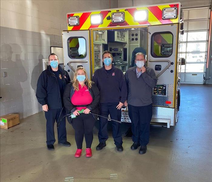 Four people in masks standing in front of a fire truck.