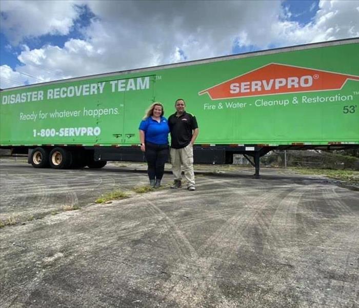 Two people in front of a SERVPRO trailer.