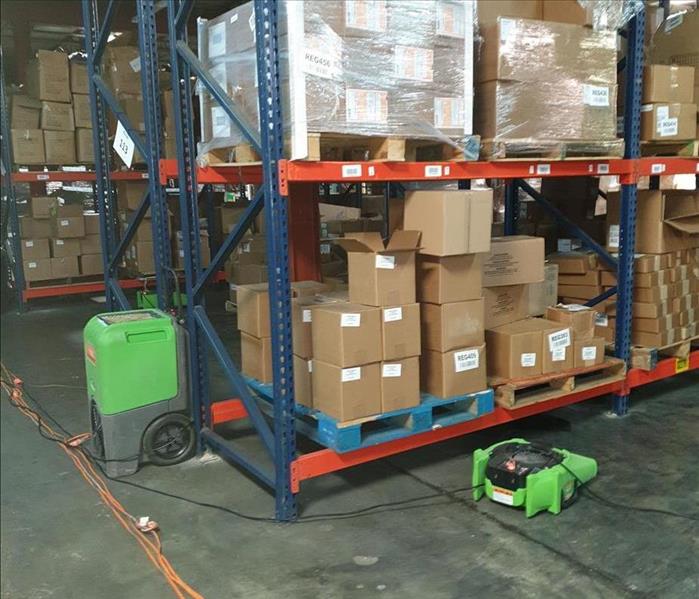 Warehouse filled with shelves and boxes. There are two green air movers on the floor.